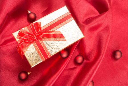 Gift box with bow, on red wavy satin fabric with Christmas balls.の写真素材