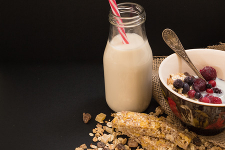 Bowl of muesli with frozen berries and bottle of plant milk, on black background.の写真素材