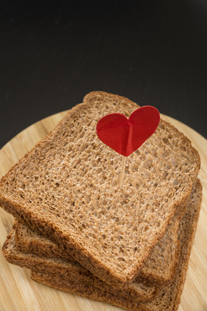 Whole grain sandwich bread slice with heart pin, with dark background.の写真素材