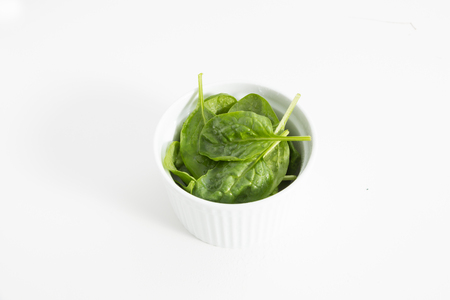 Fresh wet green baby spinach leaves in a bowl, closeup on white background.の写真素材