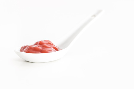 Creamy red sauce in white ceramic spoon, on white background.の写真素材