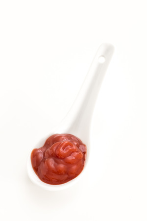 Creamy red sauce in white ceramic spoon, on white background.の写真素材