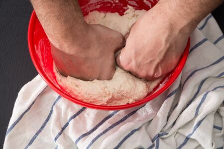 Male hands kneading dough in red bowl, baking preparation closeup.の写真素材