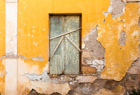 Blocked old wooden window, on yellow painted weathered wall.