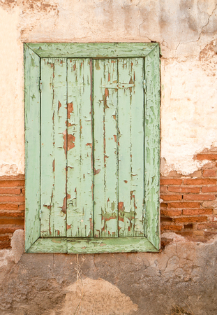 Old wooden window with green shutters on weathered wall.の写真素材