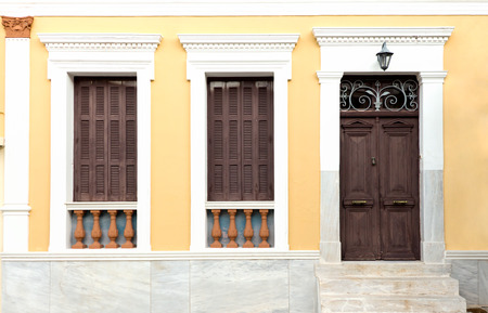 Wooden retro style door and two windows with brown shutters, on clean painted wall background.の写真素材