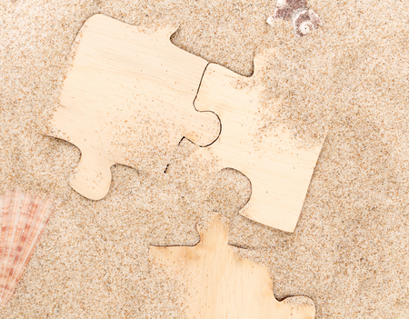 Three pieces of blank wooden puzzle , on sandy background with seashells.の写真素材