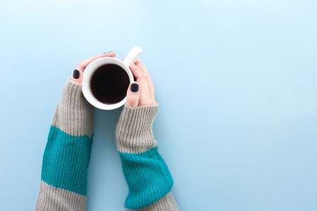 Hands holding a cup of freshly brewed black coffee, flat lay on blue background.の写真素材