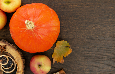 Round orange pumpkins with autumn leaf, apples and spices, flat lay on wooden background.の写真素材