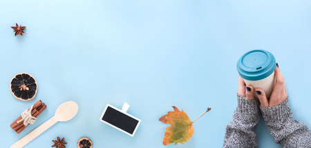 Hands holding a takeaway bamboo coffee cup, on blue background with relevant objects.の写真素材