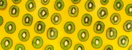 Green kiwifruit slices in lines with hard shadows on yellow background, flat lay image.の写真素材