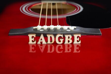 Musical notes EADGBE in corresponding to strings arrangement, with wooden letters, on reflecting surface of an acoustic guitar. Guitars bridge perspective. Creative background.の写真素材