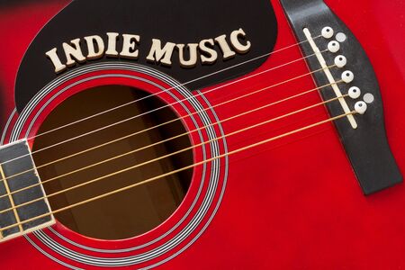 Words Indie Music with wooden letters, closeup on a surface of red acoustic guitar. Music entertainment background.の写真素材
