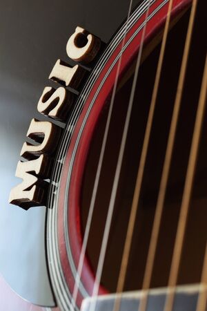 Word Music with wooden letters, closeup on a surface of red acoustic guitar. Music entertainment background.の写真素材
