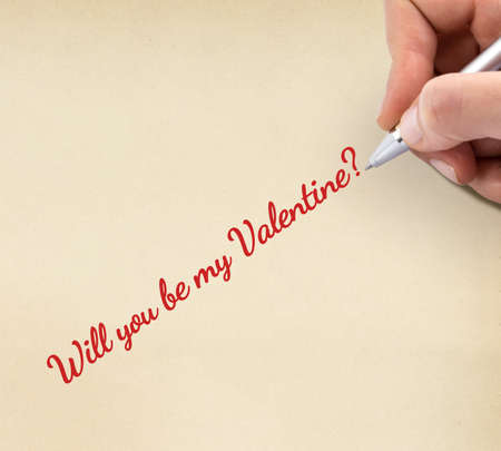 Hand writing "Will you be my Valentine?" on yellow sheet of paper.の写真素材