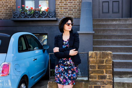 Woman in blue flowered dress, sunglasses and hat standing on the street of London.の写真素材