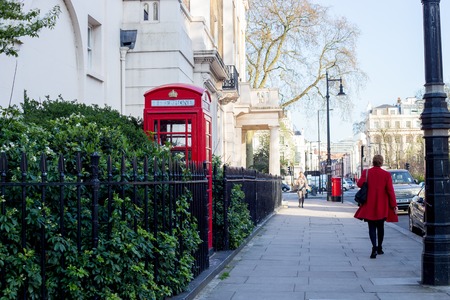 LONDON. Red telephone box on the  street. Woman in a red coat walking down the street next to a red...