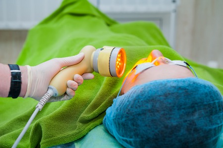 Beautiful female patient in safety glasses is getting a face skin treatment while lying at cosmeticians office, close upの写真素材