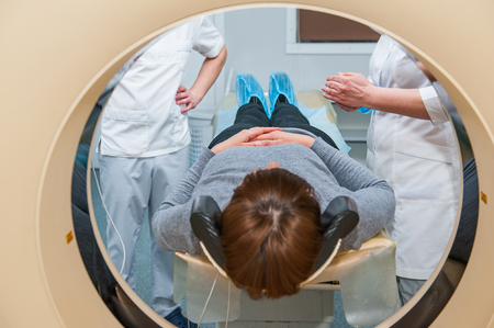 Doctor and assistant prepeared female patient for computed tomography or computed axial tomography procedure in hospital room. Shot through the tube of device. Selective focusの写真素材