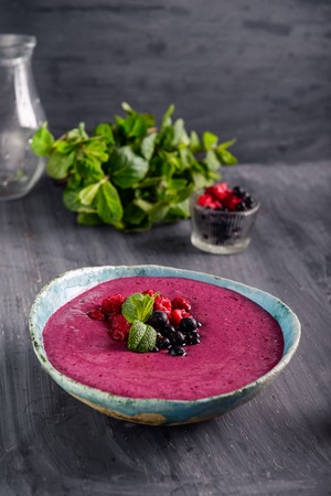 Ceramic bowl with berry smoothie decorated with currant, raspberry and mint on the black wooden background - Well being, Healthy eating, Detox or Diet concept. Selective focusの写真素材
