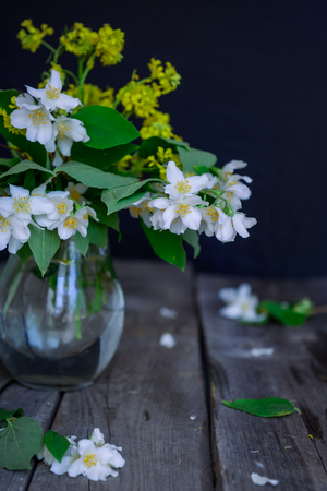Stilllife card with jasmine flowers in glass jar, separate branches with flowers and petals on the wooden rustic table. Soft selective focusの写真素材