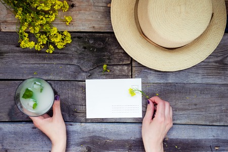 Countryside travel and vacation background. Female hands holding postcard surrounded with glass of...