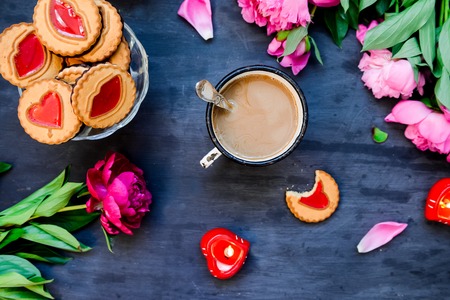 The concept of morning coffee in a romantic style on the black wooden background. Peonies flowers and petals, cookies, heart candles, mug with coffee . Valentine's love day. Top viewの写真素材