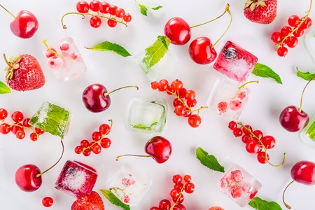 Top view ice cubes with fresh berries among not frozen cherry, strawberry and mint leafs on the white background. Selective focusの写真素材
