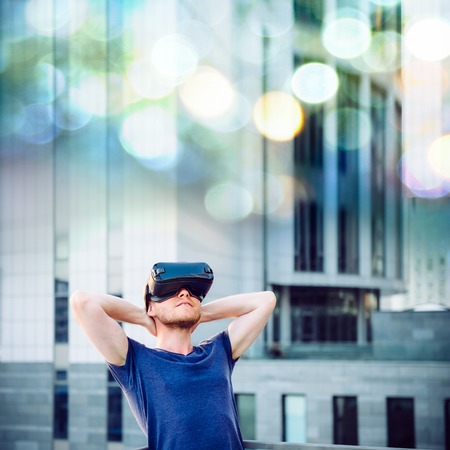 Young man enjoying virtual reality glasses headset or 3d spectacles looking up and standing against...