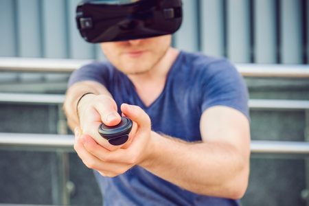 Young man pressing the control panel button enjoying virtual reality glasses or 3d spectacles on the urban building background outdoors. Technology, innovation, cyberspace and gaming. Selective focus.の写真素材