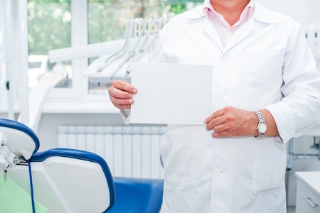 Male Dentist doctor holding empty blank with his recommendations in his dental office. Medical service and Healthy life concept. Space for text. Selective focusの写真素材