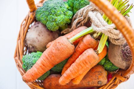 Straw Basket with garden Vegetables - fresh carrots, beets, broccoli, onions on the white wooden background. Farm Harvest. Food or Healthy diet concept.Vegetarian.Copy space for Text, .selective focus.の写真素材