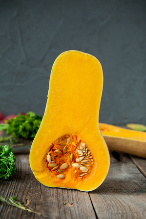 Part of ripe orange pumpkin with seeds standing on the rustic wooden table on the dark grey stone background. Vegetarian, vegan, healthy diet food. Autumn harvest. Selective focus. Space for textの写真素材