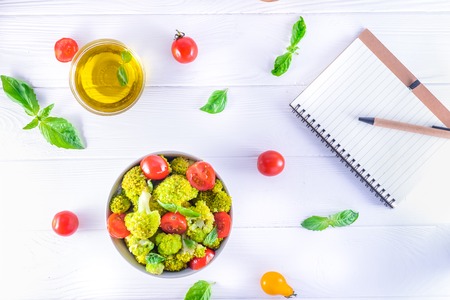 Top view Salad Bowl with cherry tomatoes, and broccoli and diet notebook on the white wooden background. Healthy lifestyle concept. Detox, diet, vegitarian. Selective focus. Text spaceの写真素材