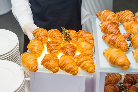 The waiter is servering catering buffet table with food and snacks for guests of the event. Dining Food Celebration Party Concept. Service at business meeting, weddings. Selective focus.の写真素材