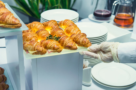 The waiter is servering catering buffet table with food and snacks for guests of the event. Dining Food Celebration Party Concept. Service at business meeting, weddings. Selective focus.の写真素材