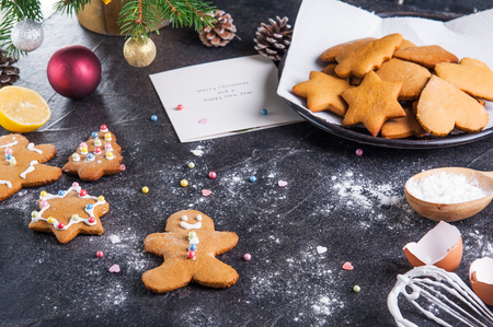 Christmas homemade gingerbread cookies and postcard on the black stone background, new year holiday concept. The process of decorating with meringue cream. Selective focus. Space for text, top viewの写真素材