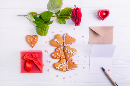 Homemade cookies in shape of heart with I Love you words as gift for lover on Valentine's day. White wooden table with greeting card, rose and decor. Festive gift concept. Selective focus. Copy space.の写真素材