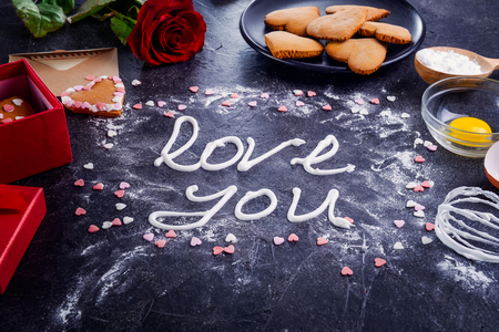 Top view meringue cream lettering Love you on the black stone background with ingredients, flower, gift box with cookies and decor details. Valentine's day concept. Gift for lover. Selective focusの写真素材