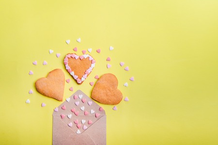 Open craft paper envelope with fly out sugar candies and heart shaped homemade cookies on bright yellow background. Valentine day. love concept. Gift, message for lover. Space for textの写真素材