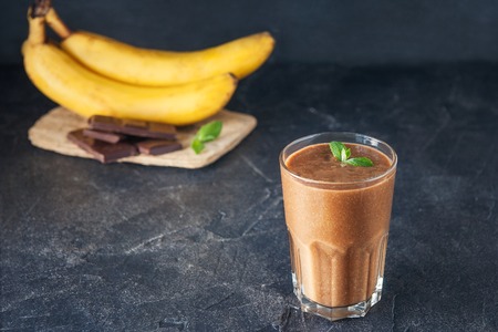 Glass of fruit banana-chocolate smoothie with mint leaves and ingridients on the dark background. Healthy, vegetarian, vegan diet food. Selective focus, space for textの写真素材