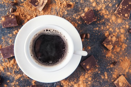 Top view cup of black coffee on a dark stone background with beans, cocoa powder and chocolate pieces scattered around. Selective focus. Space for textの写真素材