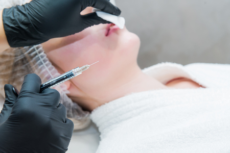Contour plastic: Dermatologist doctor inject filler. Close up female hands of cosmetologist making injection in lips. Aesthetic cosmetology. Selective focus.の写真素材