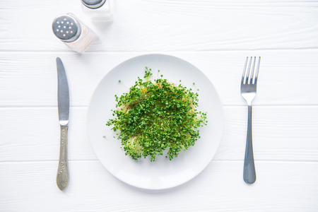 Top view plate with fresh organic sprout micro greens served with cutlery and herbs on the white wooden table. Healthy Raw diet food concept. Copy space for text. Selective focusの写真素材