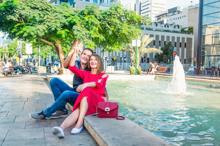 Romantic couple sitting on the bench near the city fountain and enjoying moments of happiness. Love, dating, romance. Lifestyle and tourism concepts. Selective focus. Copy spaceのeditorial素材