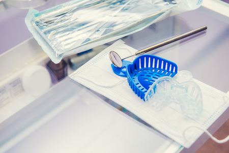 Set of packaged sterilized medical equipment tools, dentist s mirrow and jaw molds on mask on the working table in orthodontic clinic. Selective focus, space for text.の写真素材
