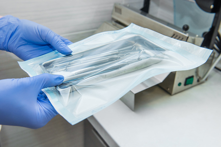 Close up dentist assistants hands holding packaged with vacuum packing machine medical instruments ready for sterilizing in autoclave. Dental office. Selective focus, space for text.の写真素材