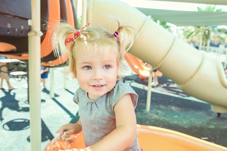 Portrait of emotional smiling little blondy baby girl climbing on the slide on the outdoor summer...