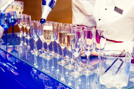 Waiter pouring personal serving Champagne in glasses on bright blue stand