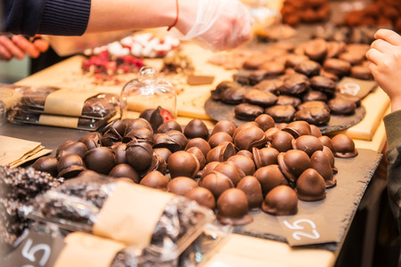Display with assortment of dark and brown chocolate candies with different fillings. Seller's hand picks some slice for buyer testing. Tasty and delicious desserts. Selective focusの写真素材